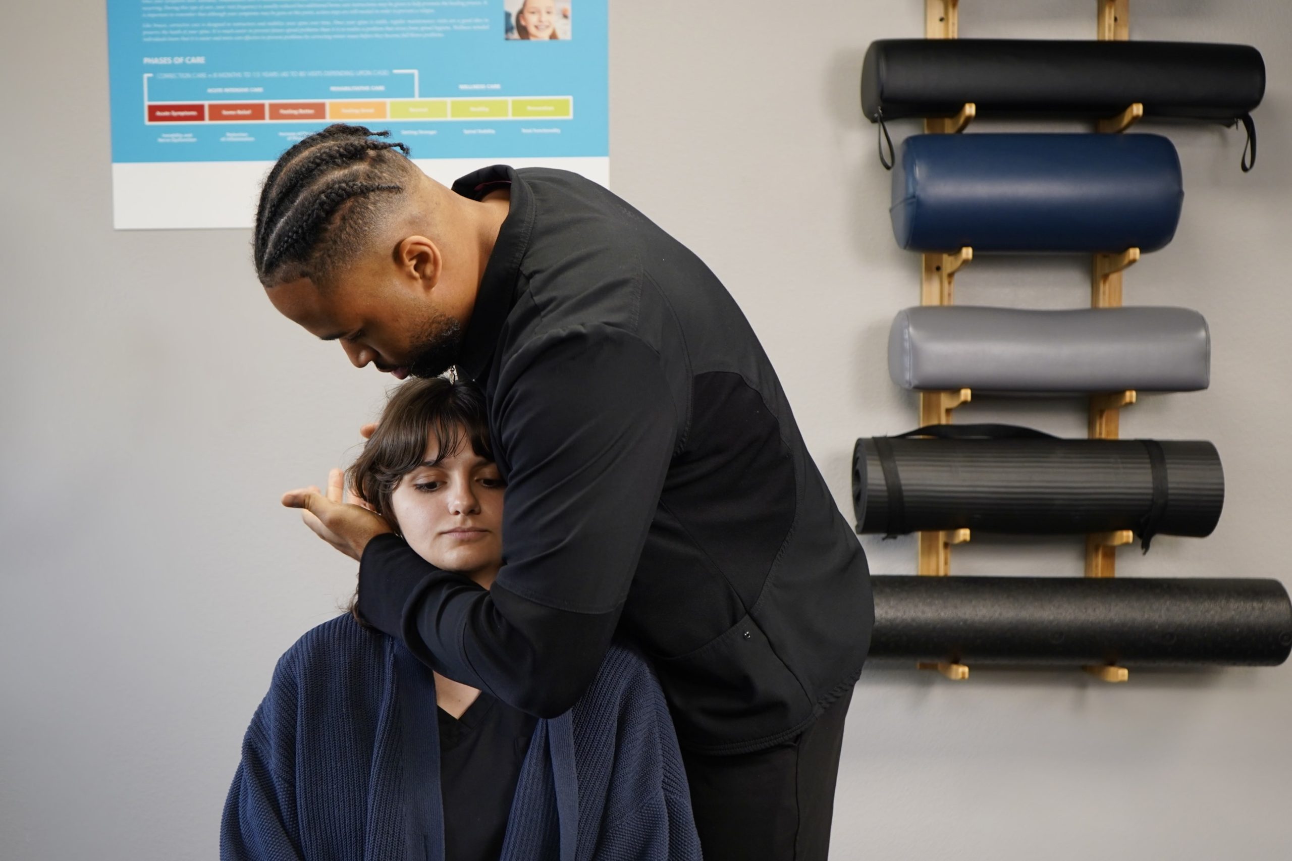 a man adjusts a woman 's neck in front of a poster that says " phases of care "