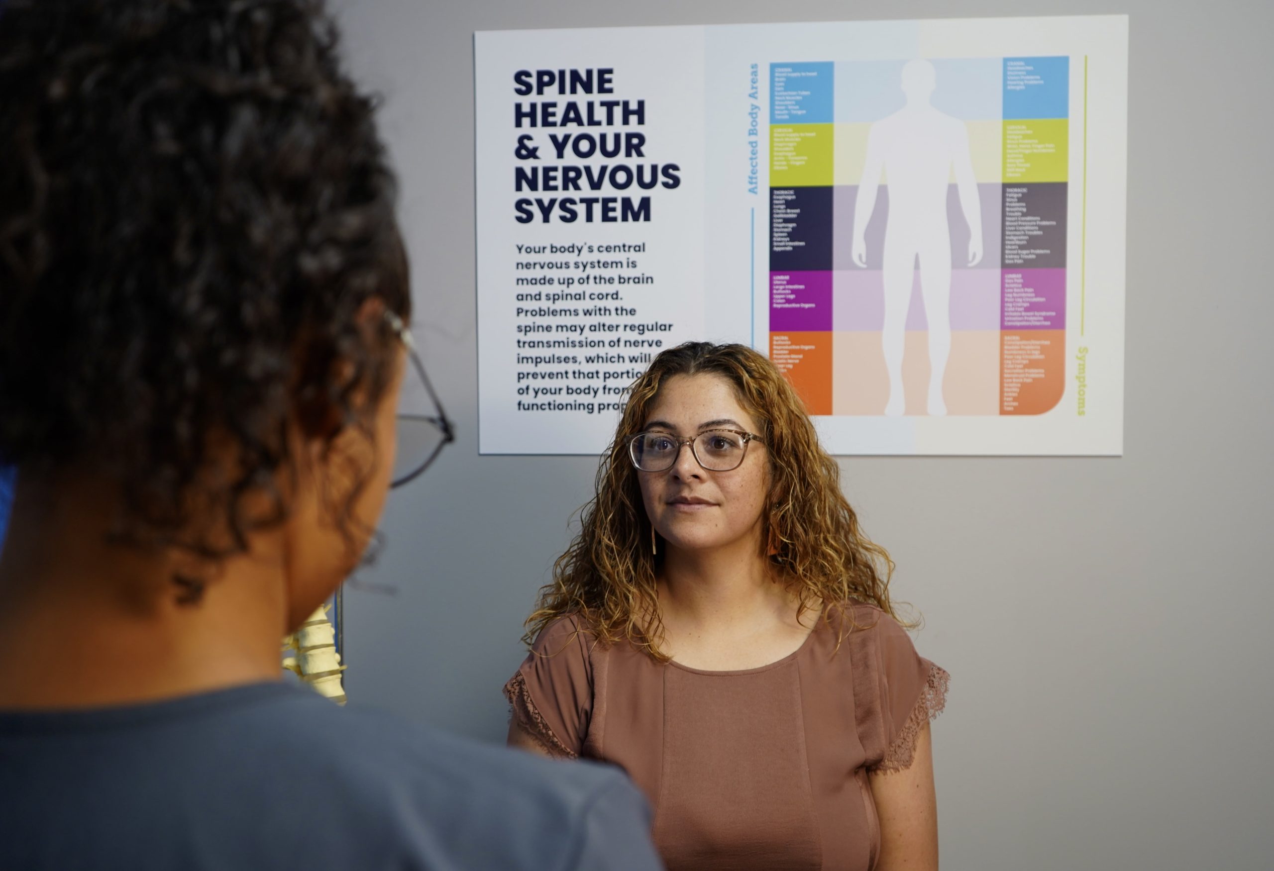 a clinician talking to a patient in front of a poster that says spine health & your nervous system
